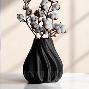 May include: A black ceramic vase with a wavy, pleated design holds a bouquet of white cotton stems. The vase is sitting on a white marble surface.
