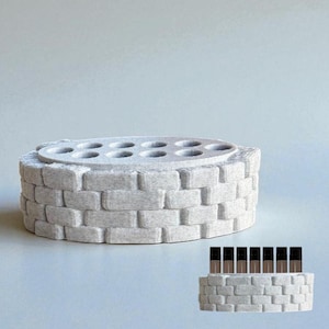 May include: A light gray, brick-patterned cosmetic organizer with a circular top featuring multiple holes. The organizer is designed to hold various beauty products, such as lipsticks or small bottles. A smaller version of the organizer is also shown.