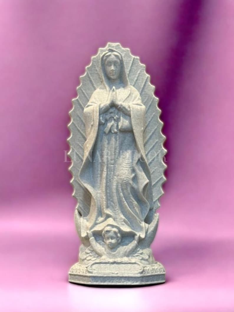 May include: A grey statue of the Virgin Mary, hands clasped in prayer, against a pink backdrop. The statue has a halo and a cherub at the base. A religious item, the statue is a representation of faith and devotion.