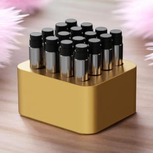 May include: A gold-colored rectangular holder with a collection of small, silver-colored vials with black caps. The vials are arranged in a grid pattern. Soft pink feather-like decorations are in the background.