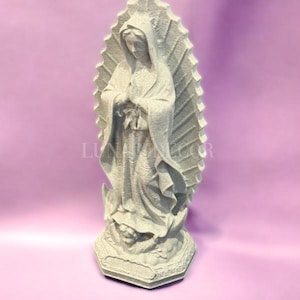 May include: A grey statue of the Virgin Mary, standing with hands clasped in prayer. The statue features a detailed depiction of her robes and a halo-like backdrop. The base is hexagonal with ornate carvings. The background is a solid light purple.