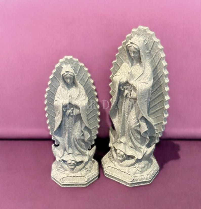 May include: Two gray Virgin Mary statues. The statues are standing, with hands clasped in prayer. Each statue has a halo-like design behind the head. The statues are on a pink background.