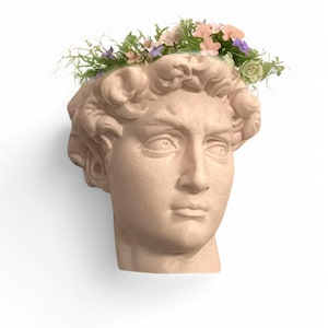 May include: A white plaster bust of a man's head with a crown of pink, purple, and white flowers.