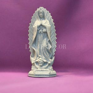 May include: A light grey statue of the Virgin Mary, with hands clasped in prayer. The statue is set against a purple background. The text "LUN DECOR" is visible on the image.