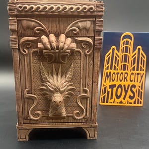 May include: A brown wooden box with intricate carvings, including a dragon head and a hand grasping a log. The box has a decorative border and is next to a yellow sign that says "MOTOR CITY TOYS".