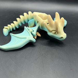 May include: A light blue and cream colored articulated dragon figurine with wings and a long tail.