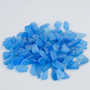 Puede incluir: Un montón de piezas de vidrio de mar azul de varias formas y tamaños. El vidrio de mar varía en tonos de azul, de claro a oscuro, con una textura esmerilada y suave. Las piezas están dispuestas sobre un fondo blanco.