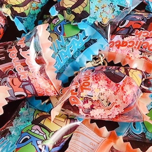 May include: A collection of clear plastic bags filled with colorful glitter and featuring cartoon images of Teenage Mutant Ninja Turtles. The bags have a scalloped edge and are labeled with the words "Dr. Touch" and "Ninja Turtle".