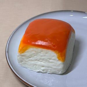 May include: A square-shaped dessert with a white base and a bright orange topping. The dessert is on a light grey plate.