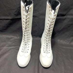 May include: A pair of white leather knee-high lace-up boots with black laces.