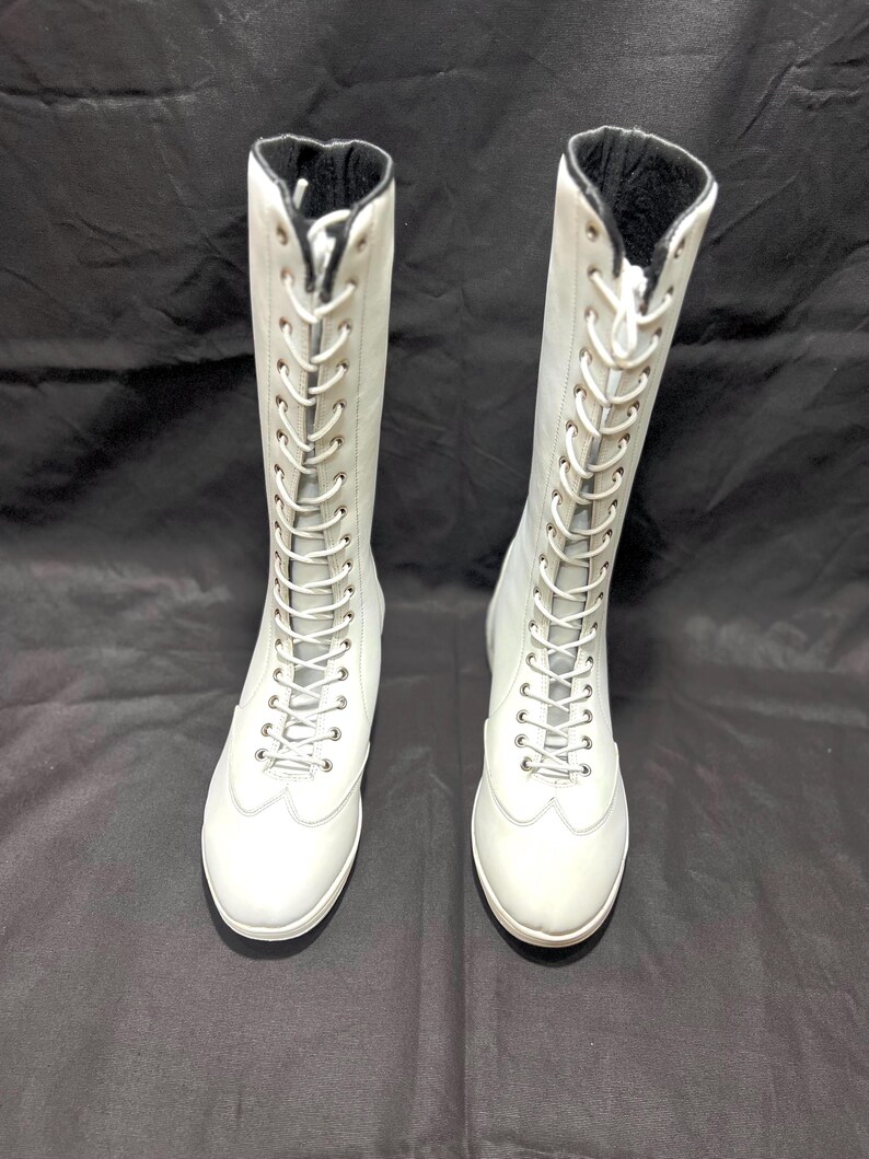 May include: A pair of white leather knee-high lace-up boots with black laces.