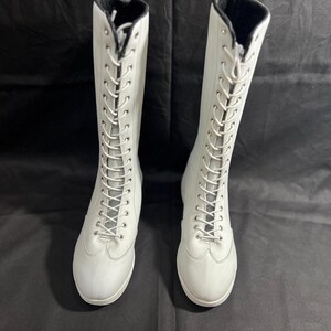 May include: Two white knee-high boots with black laces. The boots have a pointed toe and a low heel.
