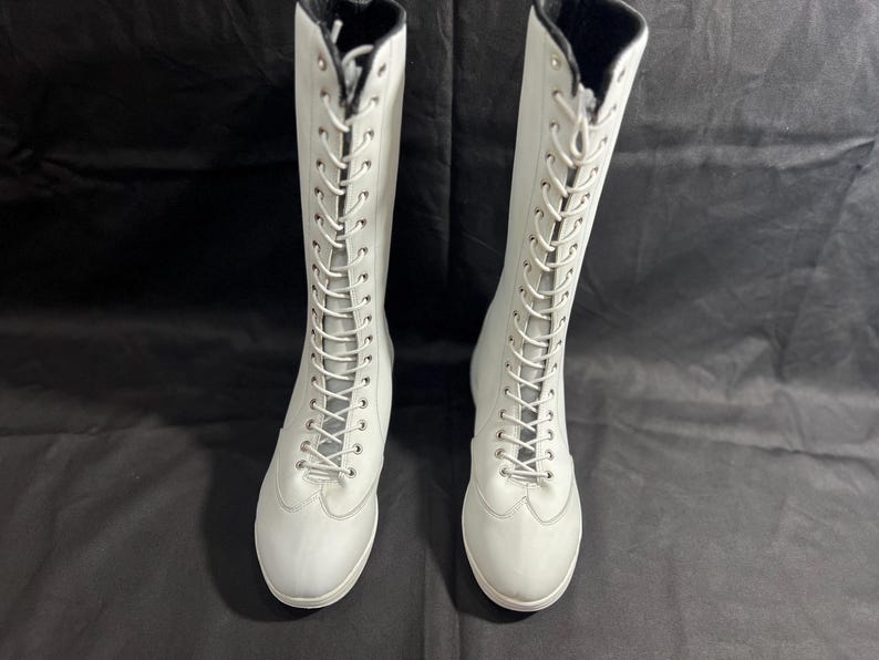 May include: Two white knee-high boots with black laces. The boots have a pointed toe and a low heel.