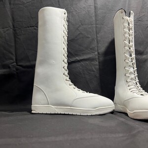 May include: Two white leather lace-up boots with white soles. The boots are tall and have a classic design.