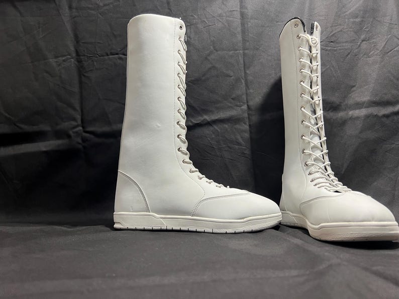 May include: Two white leather lace-up boots with white soles. The boots are tall and have a classic design.