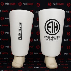 May include: Two white shin guards with the text "FAIR HAVEN" printed on them. One has the text vertically, the other has a circular logo with the text "FAIR HAVEN INDUSTRY". The guards are on a black background.