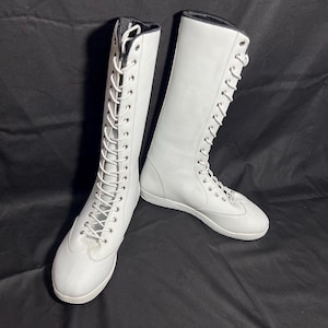 May include: Two white leather lace-up boots with white laces. The boots are tall and have a flat sole.