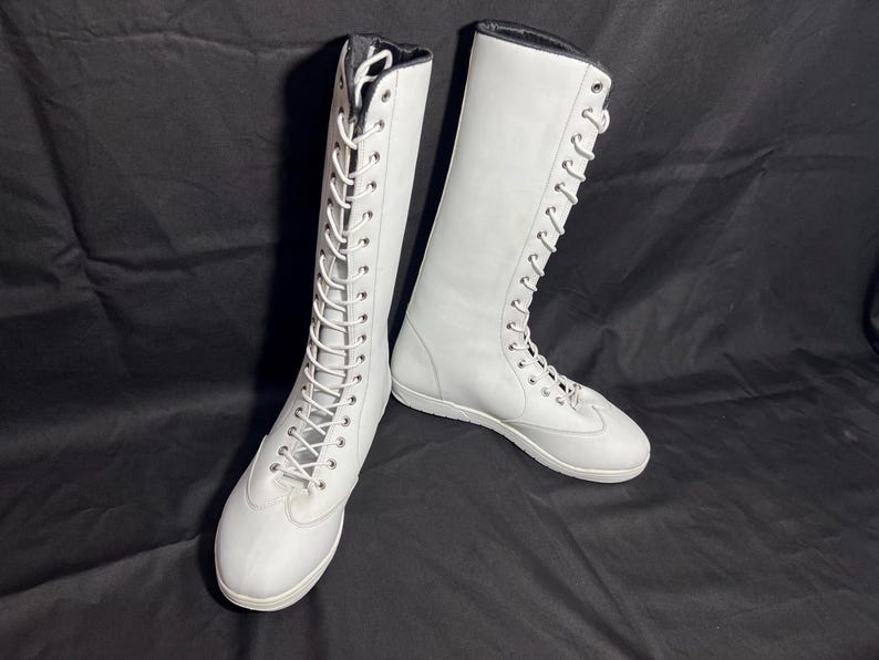 May include: Two white leather lace-up boots with white laces. The boots are tall and have a flat sole.