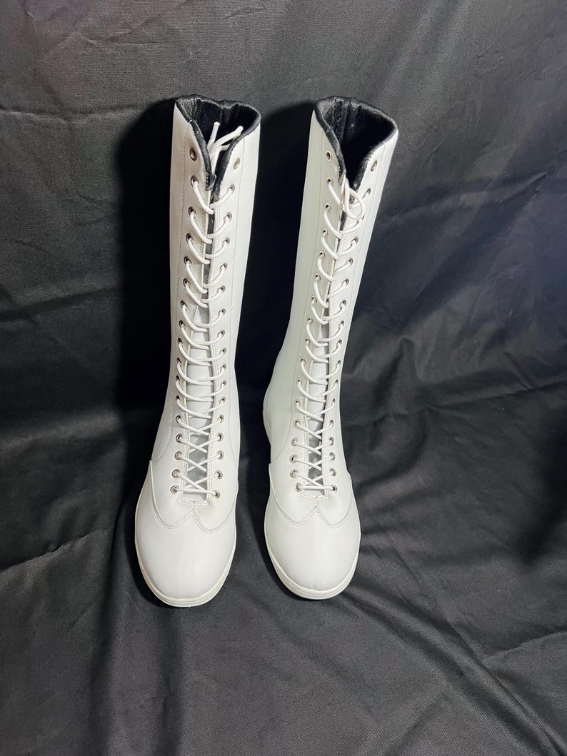 May include: A pair of white leather lace-up boots with black trim around the top of the boot.