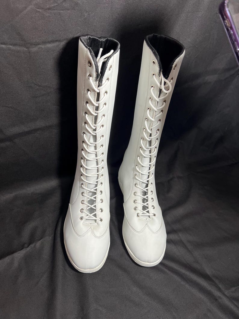 May include: A pair of white lace-up boots with black trim around the top of the boot.