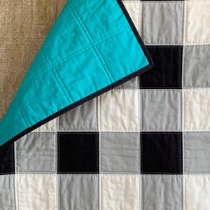 May include: A turquoise blue quilt with a black checkered pattern on the back. The quilt is made of cotton fabric and has a soft, comfortable feel.