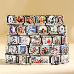 Puede incluir: Pulseras de abalorios apiladas de acero inoxidable, cada una adornada con abalorios rectangulares, ovalados y en forma de corazón. Los abalorios presentan fotografías coloridas de personas. Las pulseras se exhiben sobre una superficie beige claro.