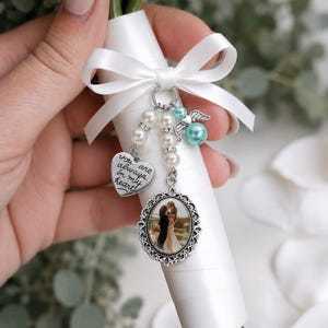 May include: A bridal bouquet charm with a photo in an ornate silver frame, a heart charm with the inscription "You are always in my heart", and pearl and turquoise beads. The bouquet is wrapped in white ribbon.