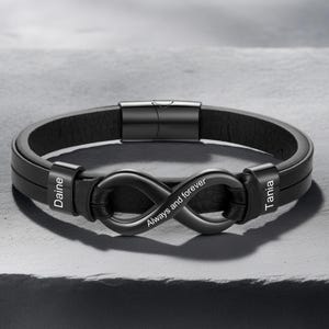 May include: Black leather bracelet featuring a black infinity symbol and magnetic clasp. The infinity symbol is engraved with "Always and forever". The bracelet has the names "Daine" and "Tania" engraved on the sides.