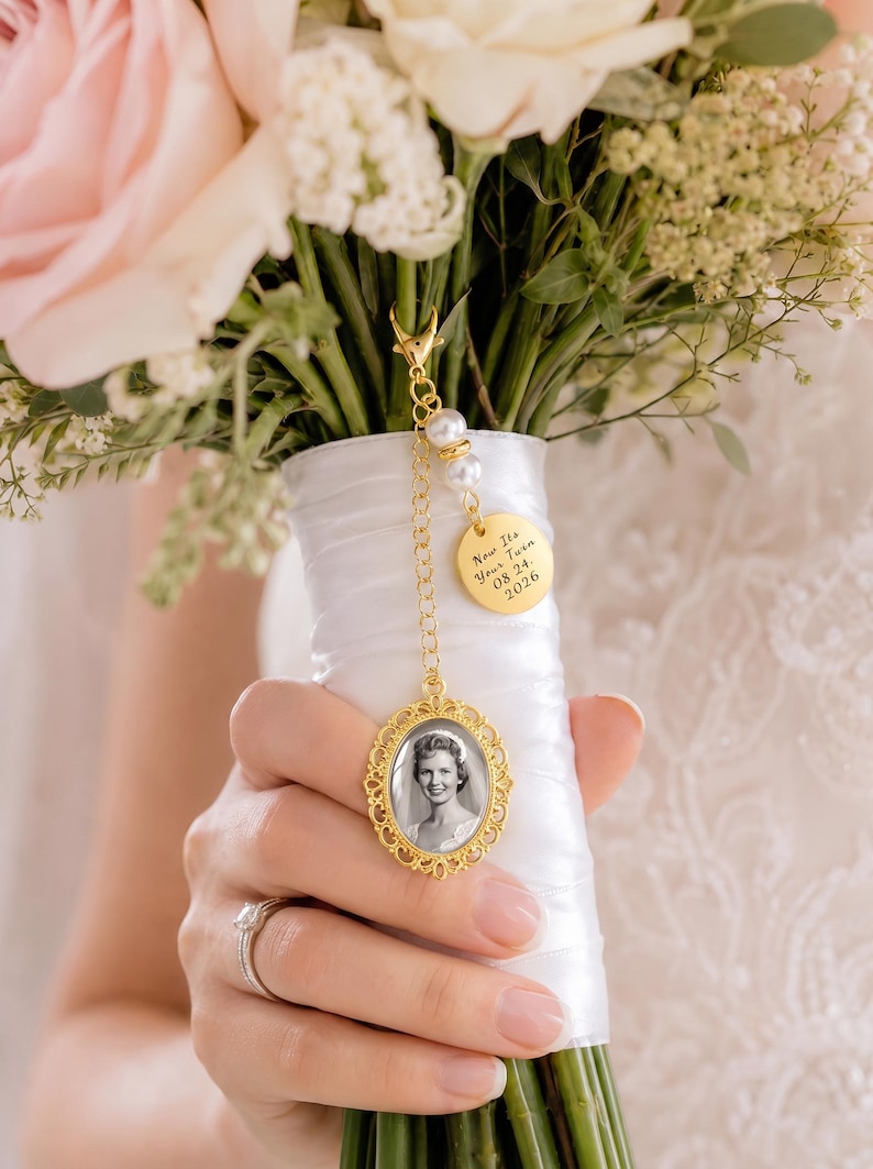 May include: A gold-toned metal photo charm featuring an oval frame with an ornate filigree border, a small round disc engraved with the text "Now Its Your Turn 08 24 2026", and two white faux pearls, all attached to a delicate chain with a lobster clasp.