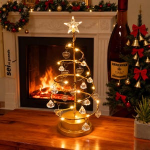 Puede incluir: Una decoración de árbol de Navidad en espiral de tono dorado con luces LED integradas, adornos transparentes tipo cristal y colgantes en forma de corazón. La estructura está rematada con una estrella brillante.