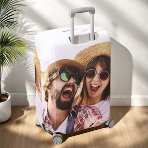 Puede incluir: Funda de maleta blanca con una imagen vibrante de dos personas con gafas de sol y sombreros de paja, en pleno selfie. Equipaje con asa retráctil y cuatro ruedas, ideal para viajar.