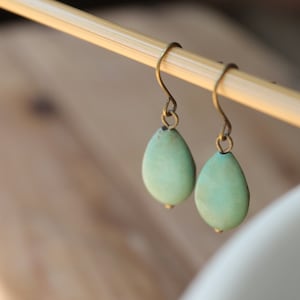 May include: A pair of turquoise teardrop earrings with brass hooks.