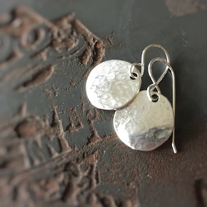 May include: A pair of silver earrings with hammered round discs. The earrings have a simple wire hook closure.