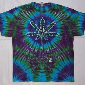 May include: A tie-dye t-shirt with a green marijuana leaf design in the center. The shirt is blue, green, and purple.