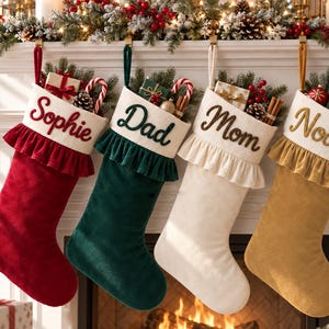 May include: Four Christmas stockings in red, dark green, cream, and gold, each featuring a ruffled cuff and embroidered names: Sophie, Dad, Mom, and Noah. The stockings are filled with small gift boxes, pine branches, and candy canes.