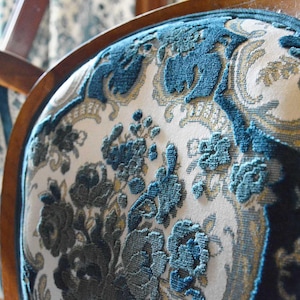 May include: Close-up of a vintage chair back with a detailed floral pattern in teal and cream. The wooden frame is visible, showcasing the chair's classic design. The fabric has a raised, textured appearance.