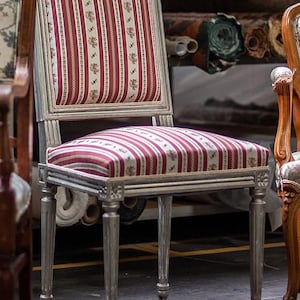Könnte beinhalten: Ein silberfarbener Stuhl mit gestreifter Sitzfläche und Rückenlehne. Der Stoff hat vertikale Streifen in Burgunderrot, Creme und Weiß mit kleinen floralen Akzenten. Der Stuhl hat geriffelte Beine und gehört zu einer Möbelkollektion.