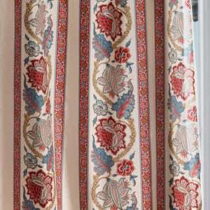 Può includere: Tessuto color crema con righe verticali e motivi floreali. Il design presenta strisce alternate di crema e rosso con dettagliati motivi floreali in rosso, blu e oro. Le tende sono vicino a una finestra con una maniglia dorata.