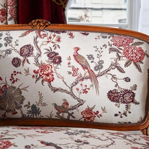 May include: A classic settee with a wooden frame and decorative elements. The cream fabric is patterned with a floral and bird design in red, burgundy, and grey. The upholstery features a pheasant and other birds.