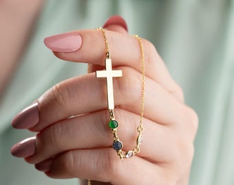 Puede incluir: Un collar de cadena de oro con un colgante de cruz y acentos de piedras preciosas verdes y azules.