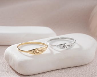 Puede incluir: Dos anillos delicados con un diseño de flor. El anillo de la izquierda es de oro y el anillo de la derecha es de plata.