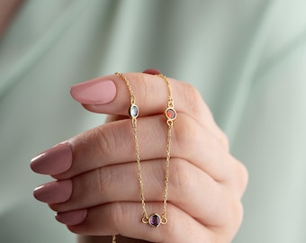 Puede incluir: Un collar de cadena de oro con tres pequeñas piedras preciosas. Las piedras preciosas son un óvalo transparente, un círculo rojo y un círculo morado.