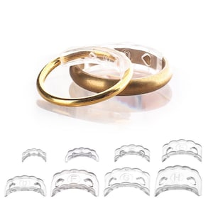 May include: Two gold rings, one with a clear plastic insert, are displayed above several clear plastic ring size adjusters. The rings have a brushed gold finish. The adjusters are labeled with letters.