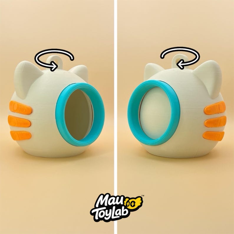May include: A spherical off-white cat-shaped toy with three orange stripes on each side, a bright blue circular opening, and a small loop on top. A black arrow indicates rotation. The text Mau ToyLab is printed at the bottom of the image.