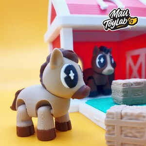 May include: A tan and brown toy horse with a stylized design, positioned in front of a red and white barn. The horse has large, expressive eyes and a jointed body. The image includes the text "Mail ToyLab".