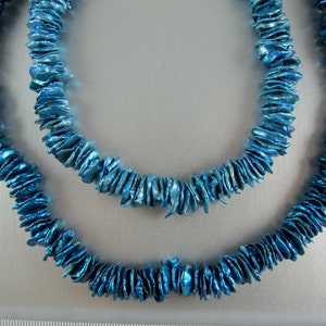 May include: Two strands of blue iridescent shell beads, each strand is a necklace, the strands are layered on top of each other.