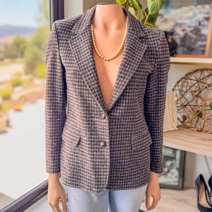 May include: A brown and black houndstooth blazer with two front pockets and a two-button closure. The blazer is displayed on a mannequin and paired with a pearl necklace. The jacket has a classic, tailored design.
