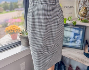 May include: A houndstooth pattern pencil skirt in black and white. The skirt has a high waist with a button closure and a tailored fit. The skirt is knee-length and made of a woven fabric.