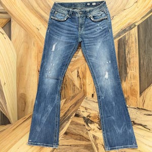May include: Blue denim jeans with a distressed wash and a slight flare at the hem. The jeans feature decorative stitching and embellishments around the pockets and waist. The jeans have a button and zipper closure.