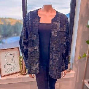 May include: A dark blue quilted jacket with a patchwork design. The jacket has a round neckline and long sleeves. The patchwork features various geometric shapes and textures. The jacket is displayed on a mannequin.